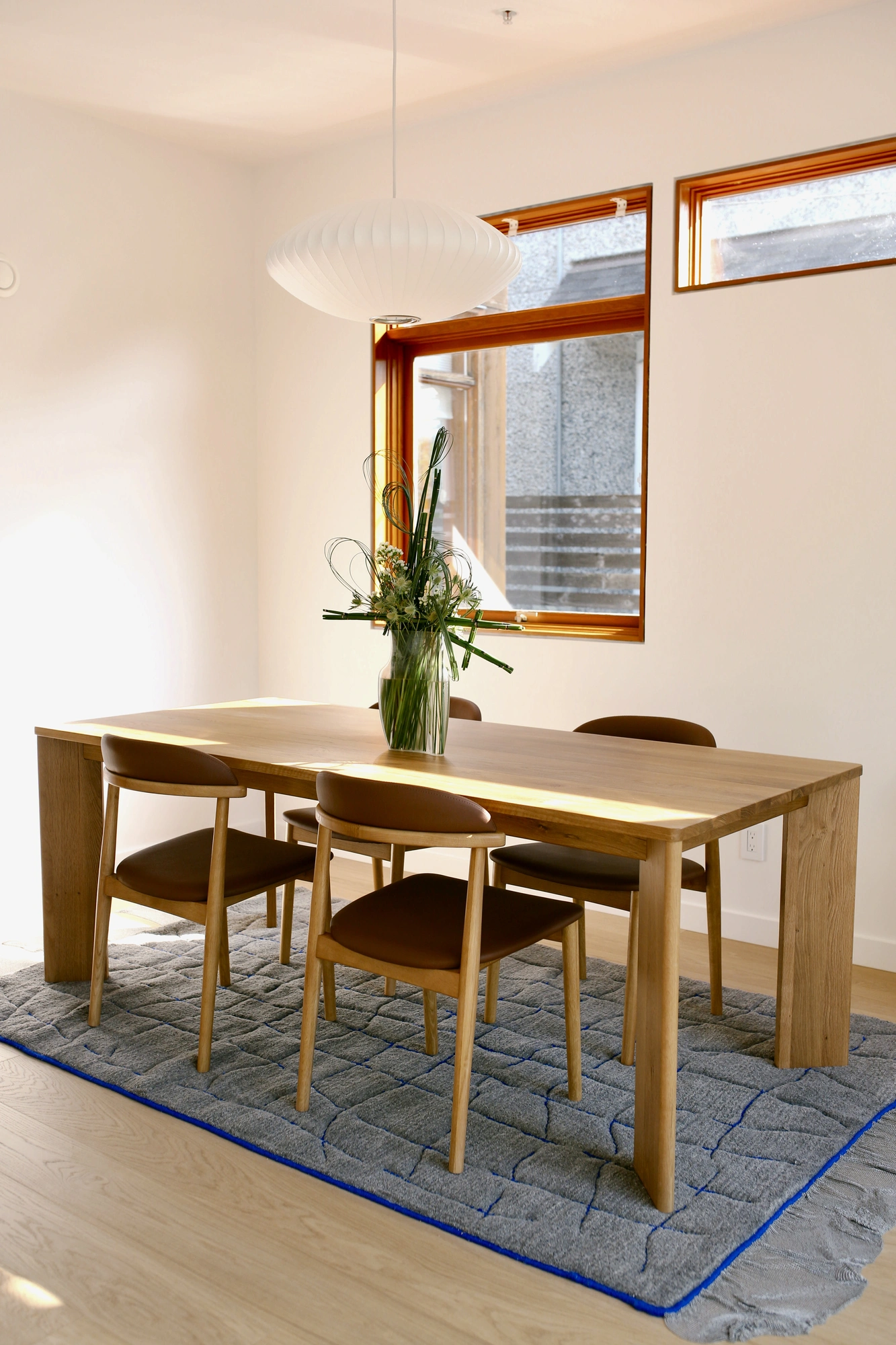Dining table arrangement with looped stems, seen across a grey rug and leather chairs