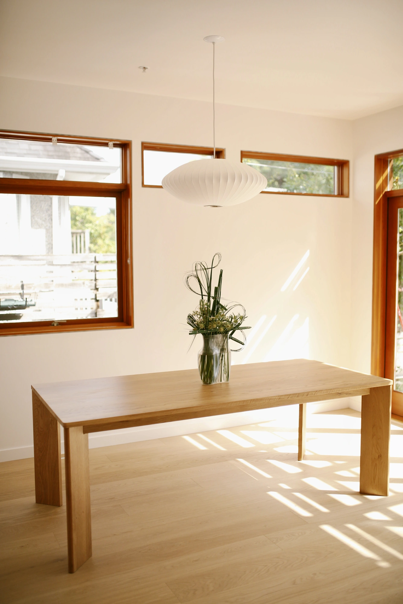 Floral arrangement in a glass vase on an oak dining table in a sunlit room