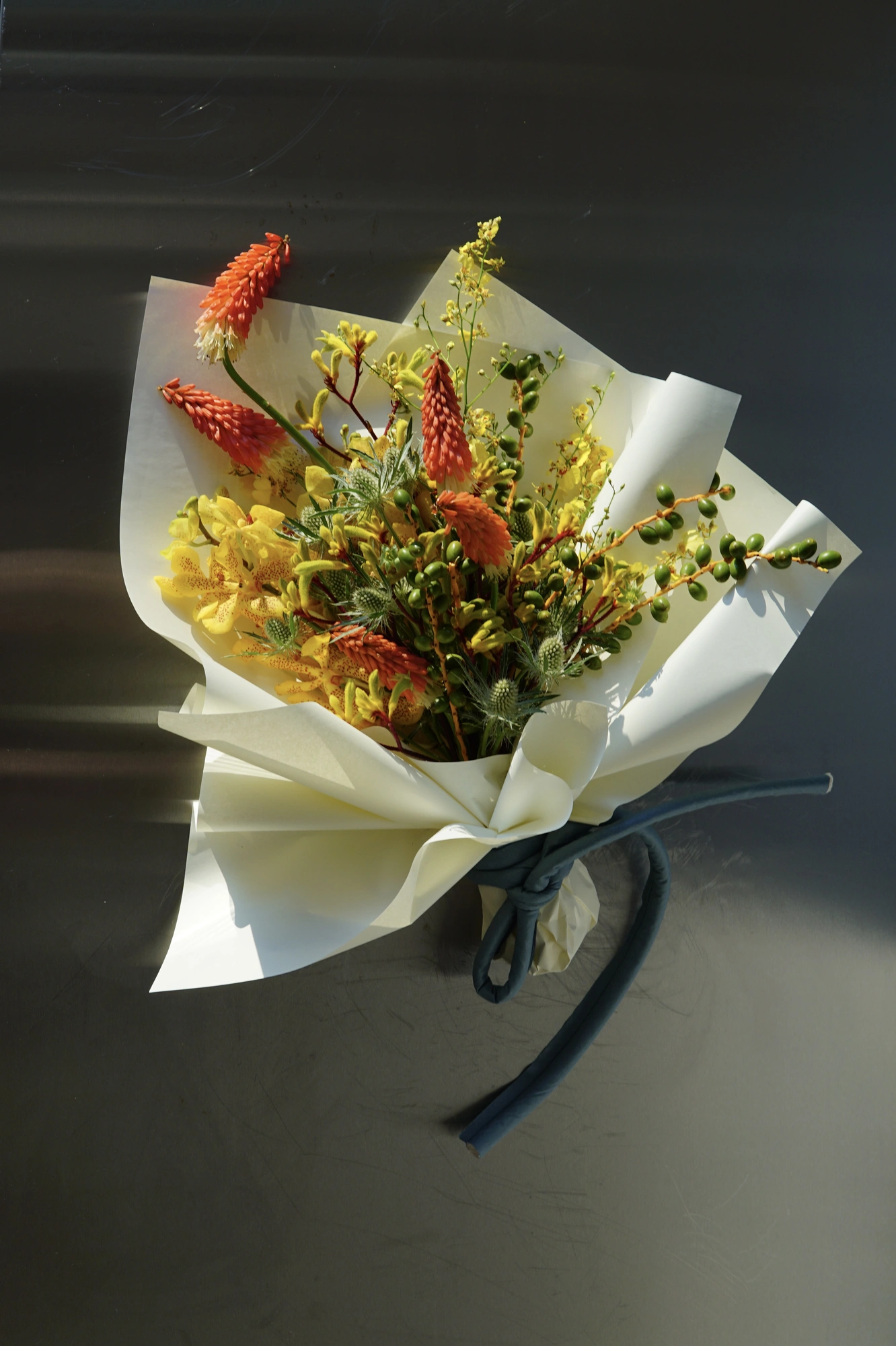 Overhead view of a wrapped bouquet with red hot poker, yellow bloom, and berry stems