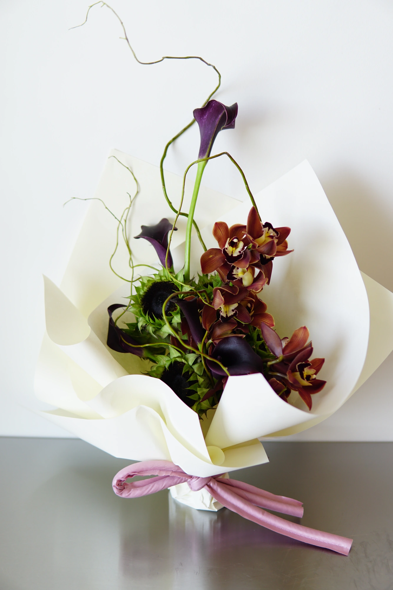 Wrapped bouquet of dark calla lilies, cymbidium orchids, and sunflower heads