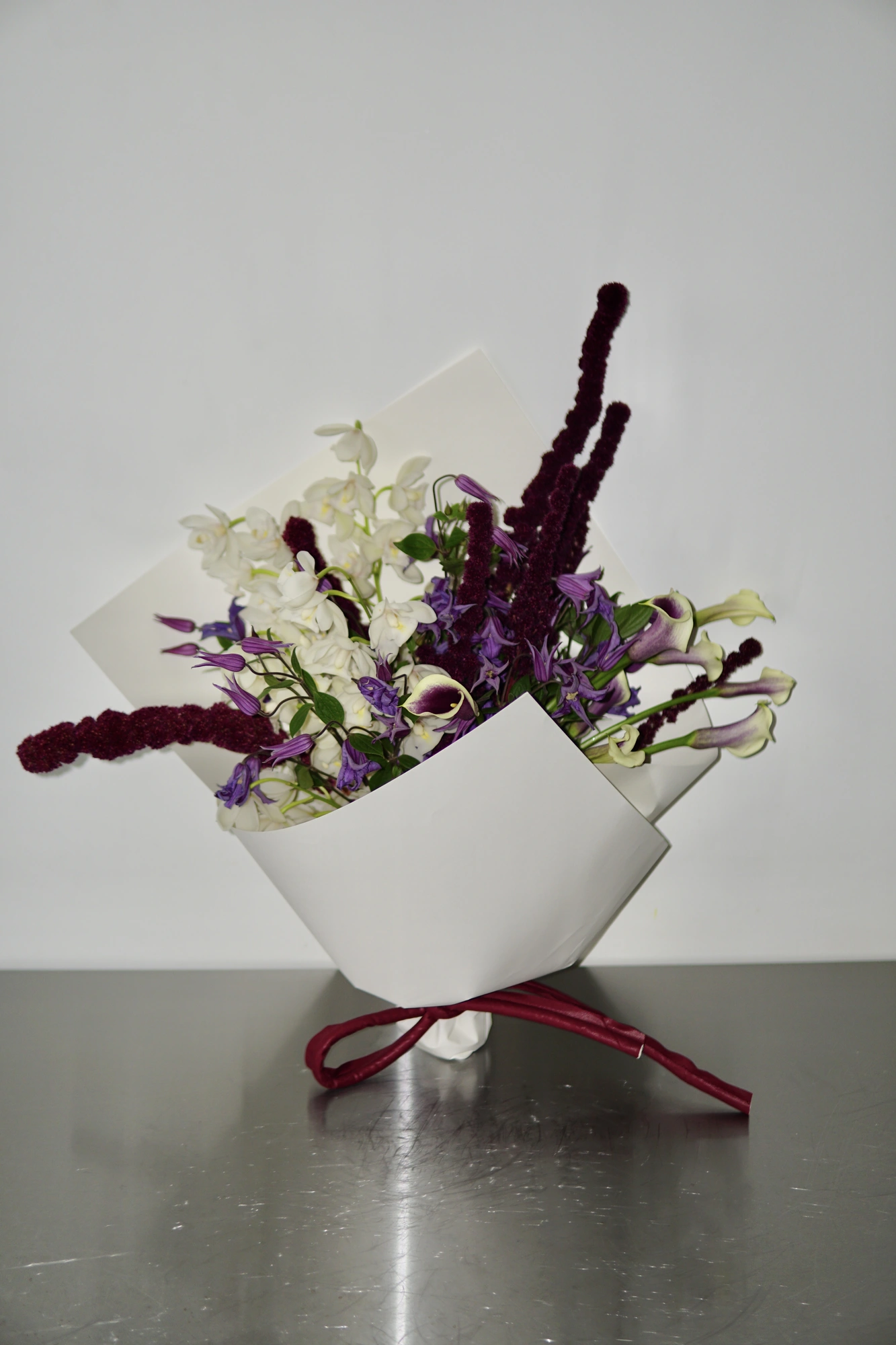 White dendrobium, clematis, and calla lilies tied with a burgundy ribbon