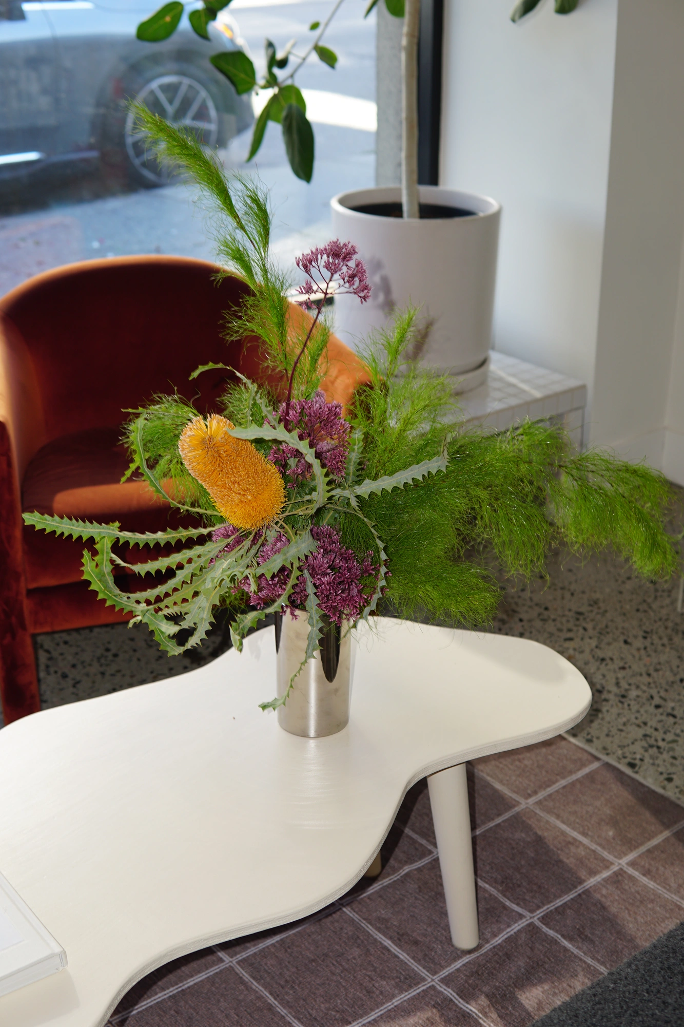 Banksia, sea holly, and asparagus fern in a steel vase at Happy Birthday Salon