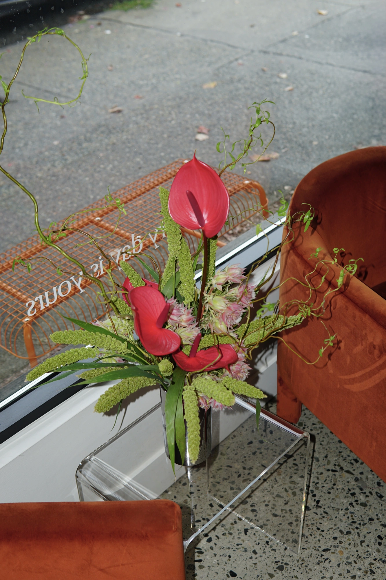 Red anthurium and amaranthus arrangement beside rust velvet chairs