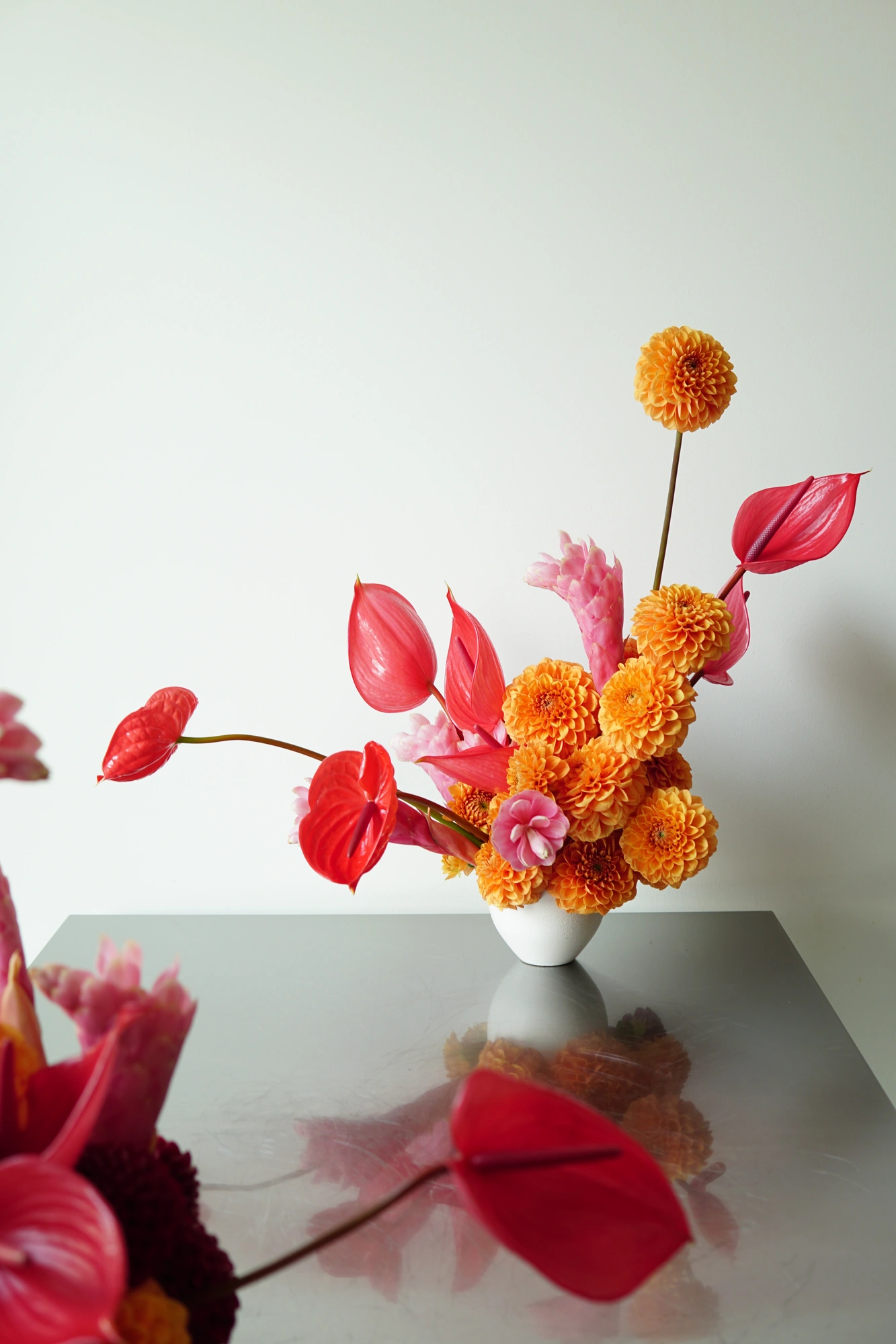 Orange dahlias and red anthurium in a white vessel on steel