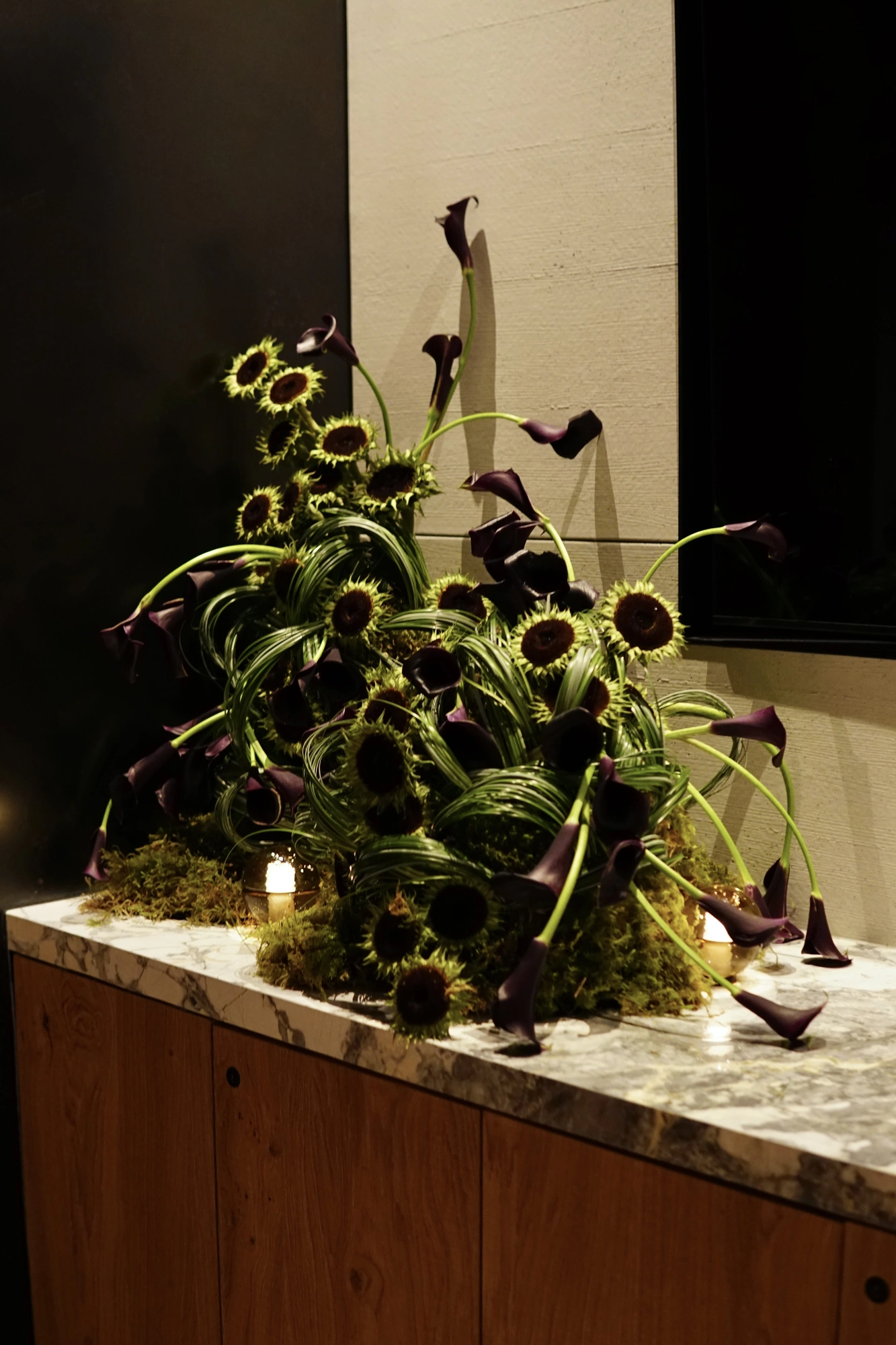 Large wedding installation of dark calla lilies and green sunflower heads on a marble console